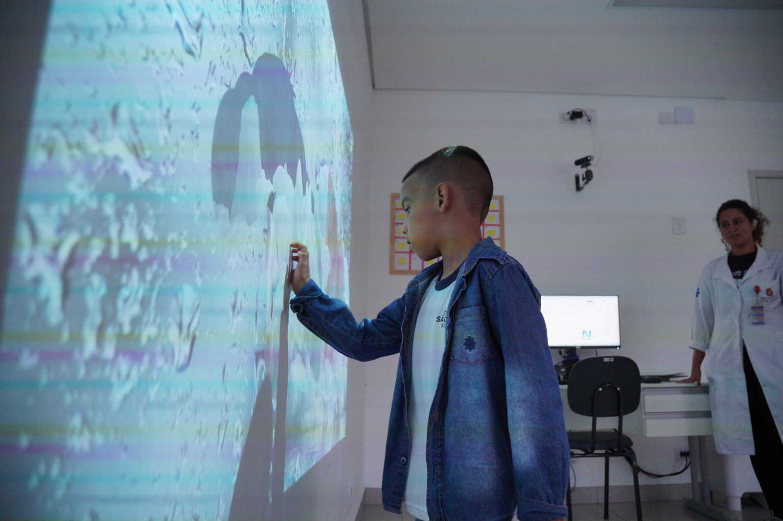 A imagem é uma montagem visual com forte distorção e repetição de elementos, criando um efeito quase caleidoscópico. É possível identificar o rosto de uma pessoa com cabelos longos e escuros, mas a imagem foi fragmentada e replicada várias vezes, sobrepondo olhos, boca e partes do rosto em diferentes posições. Isso gera uma sensação de múltiplas faces ou camadas da mesma pessoa. Ao fundo, aparecem elementos desfocados que lembram flores ou vegetação, além de partes de um ambiente interno (como uma sala), mas tudo está parcialmente encoberto pelos efeitos de edição. A parte inferior mostra mais claramente o cabelo e uma roupa azul, também distorcidos e alongados pelo efeito visual.