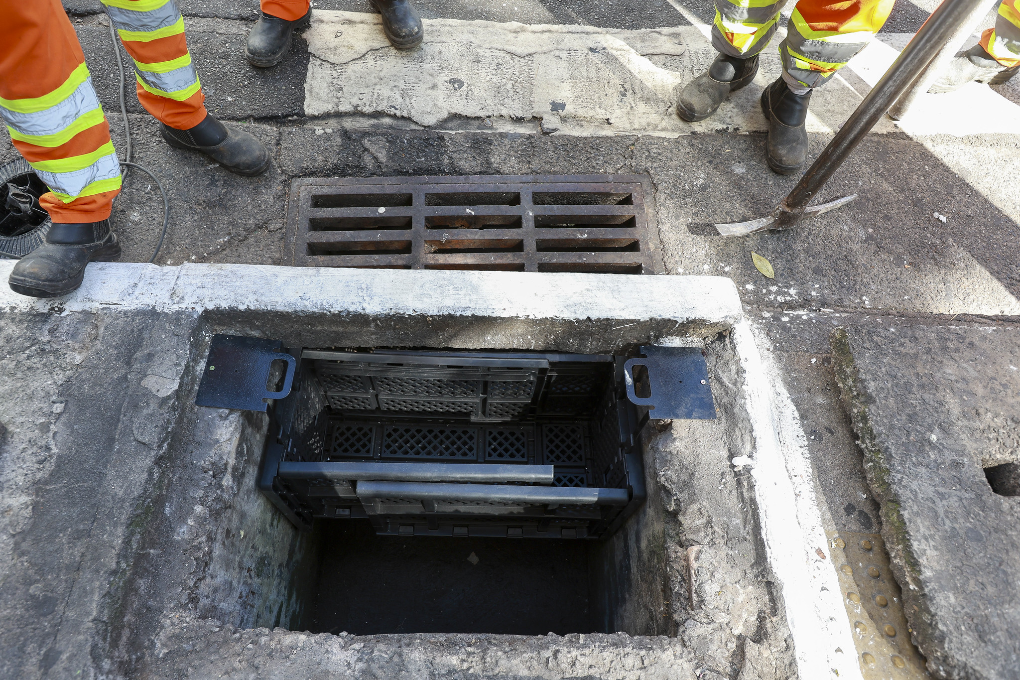 Bueiro aberto na rua, nocentro a imagem mostra um dispositivo plástico encaixado dentro do bueiro que serve como uma peneira para o lixo carregado pela água da chuva.